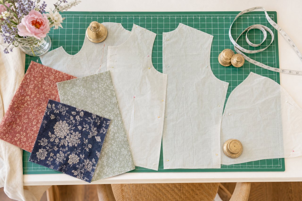 Three fabric swatches in rust, sage and navy laid across the cut pieces of a blouse pattern on a cutting mat