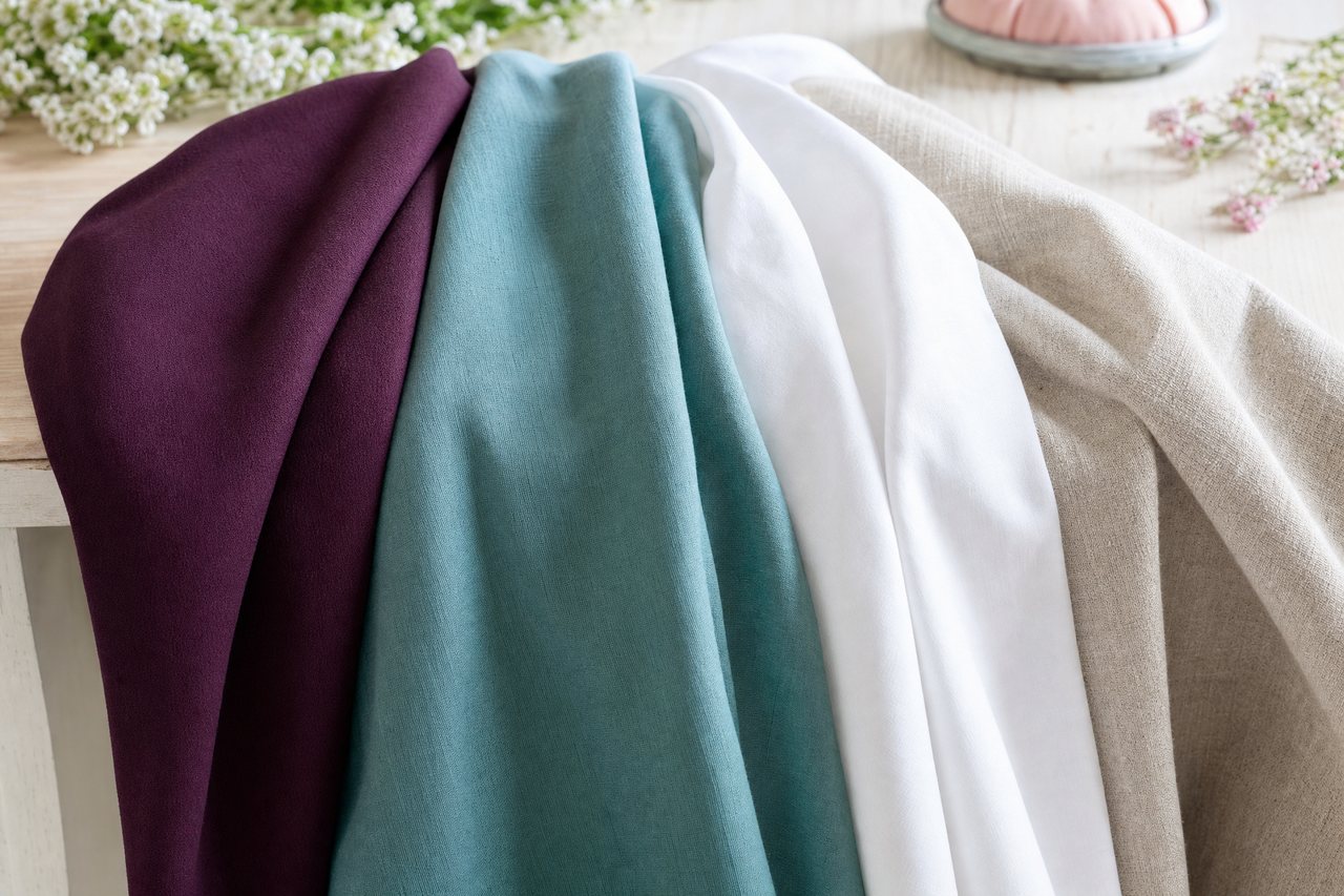Swatches of crepe, rayon challis, cotton poplin and linen fanned out on a table to compare drape