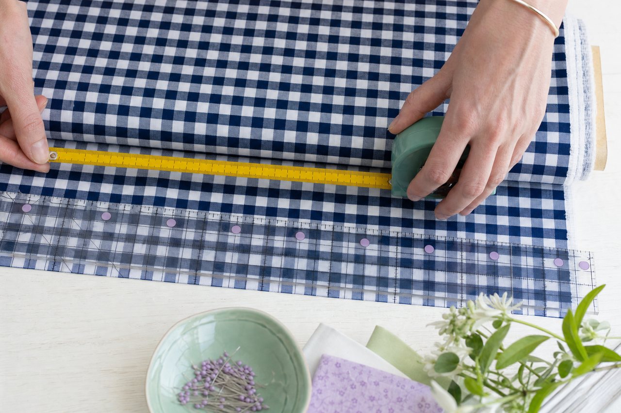 A tape measure stretched across a bolt of navy gingham beside a ruler marking the print repeat