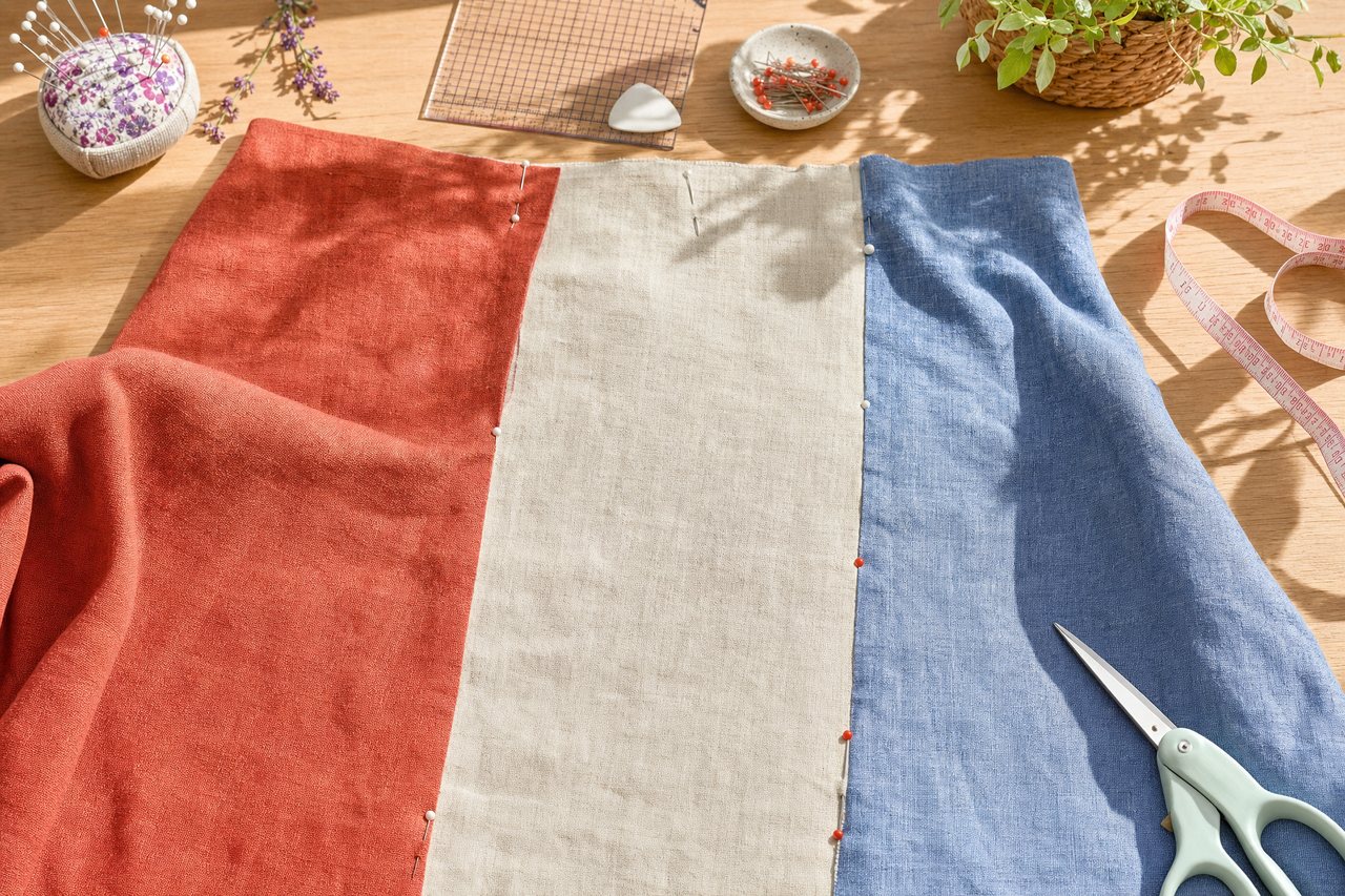 Three fabric panels in rust, cream and denim blue pinned to a dress form beside a cutting mat