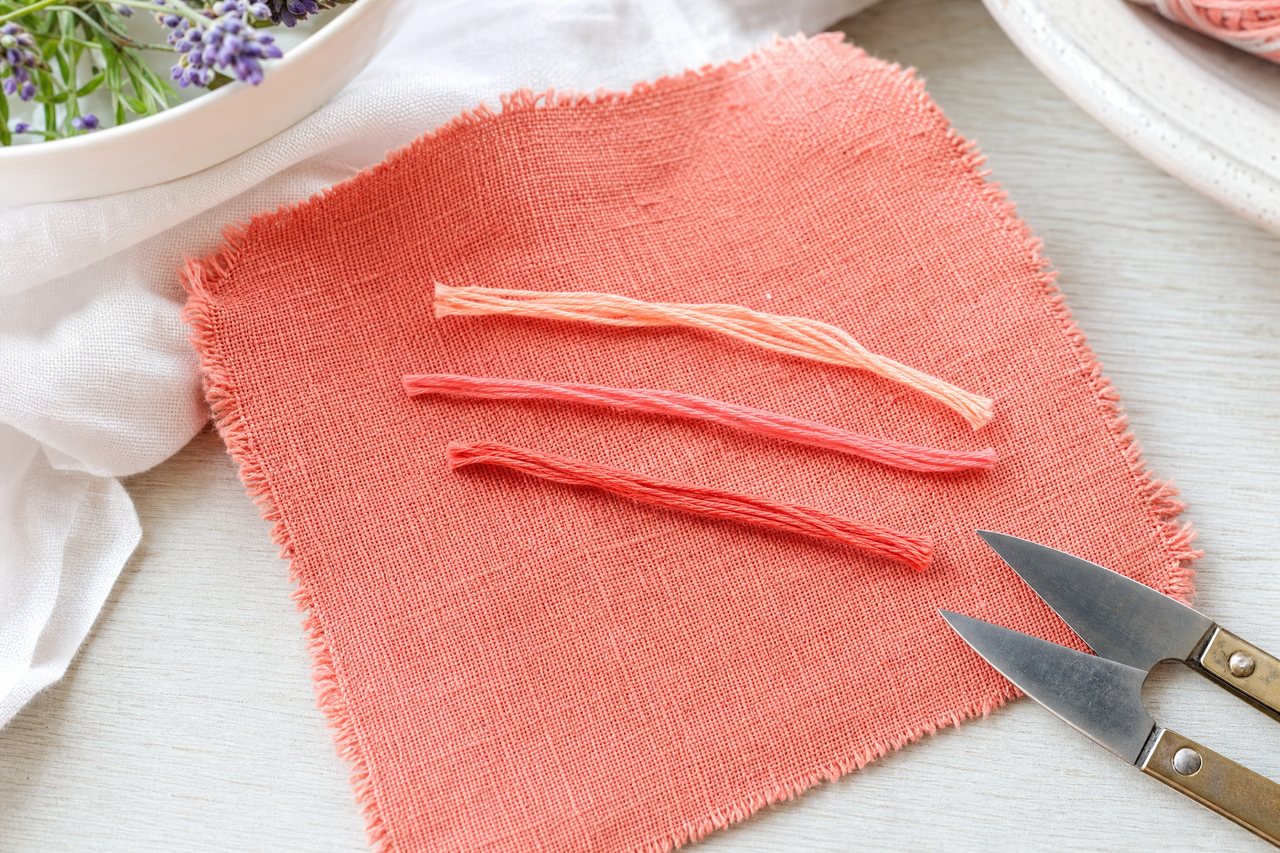 Three short strands of thread in light, matching and darker shades laid across a coral linen swatch